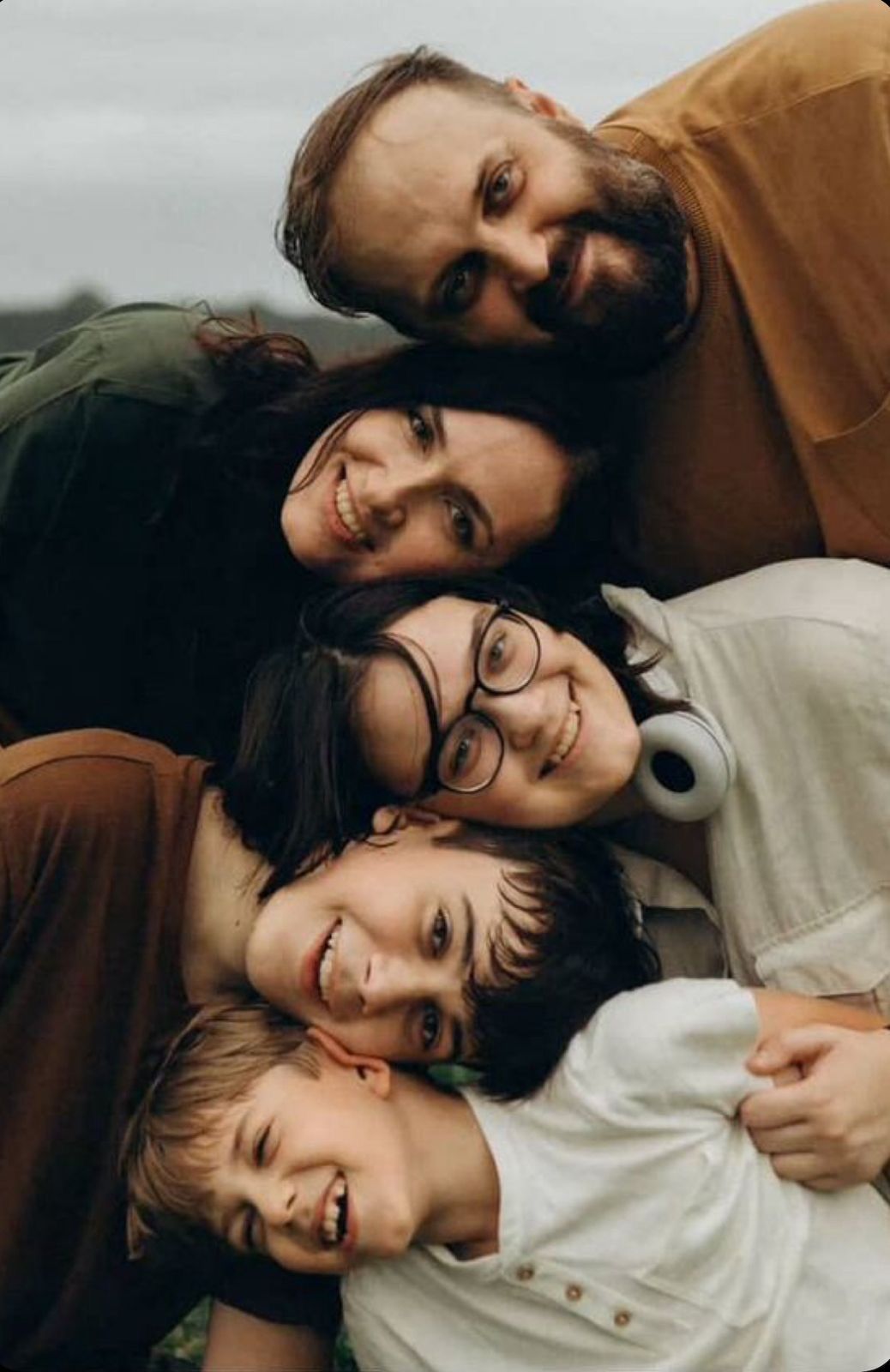 A happy family of five poses together outdoors, stacking their heads close in a warm, candid portrait.