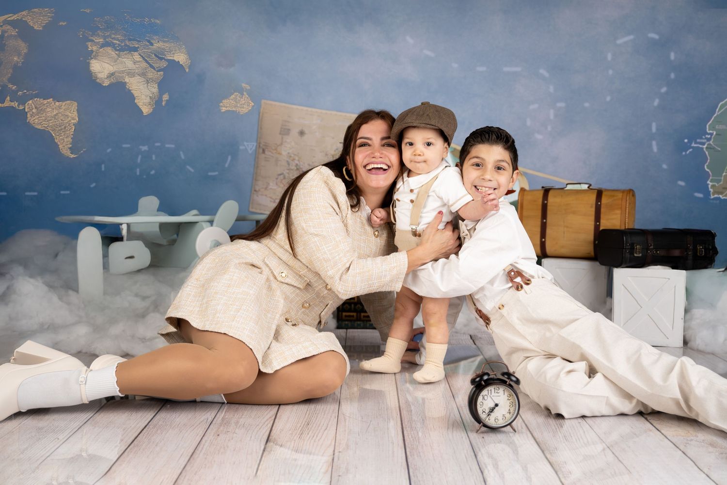 Vintage travel themed family photoshoot with world map backdrop and retro suitcase props.