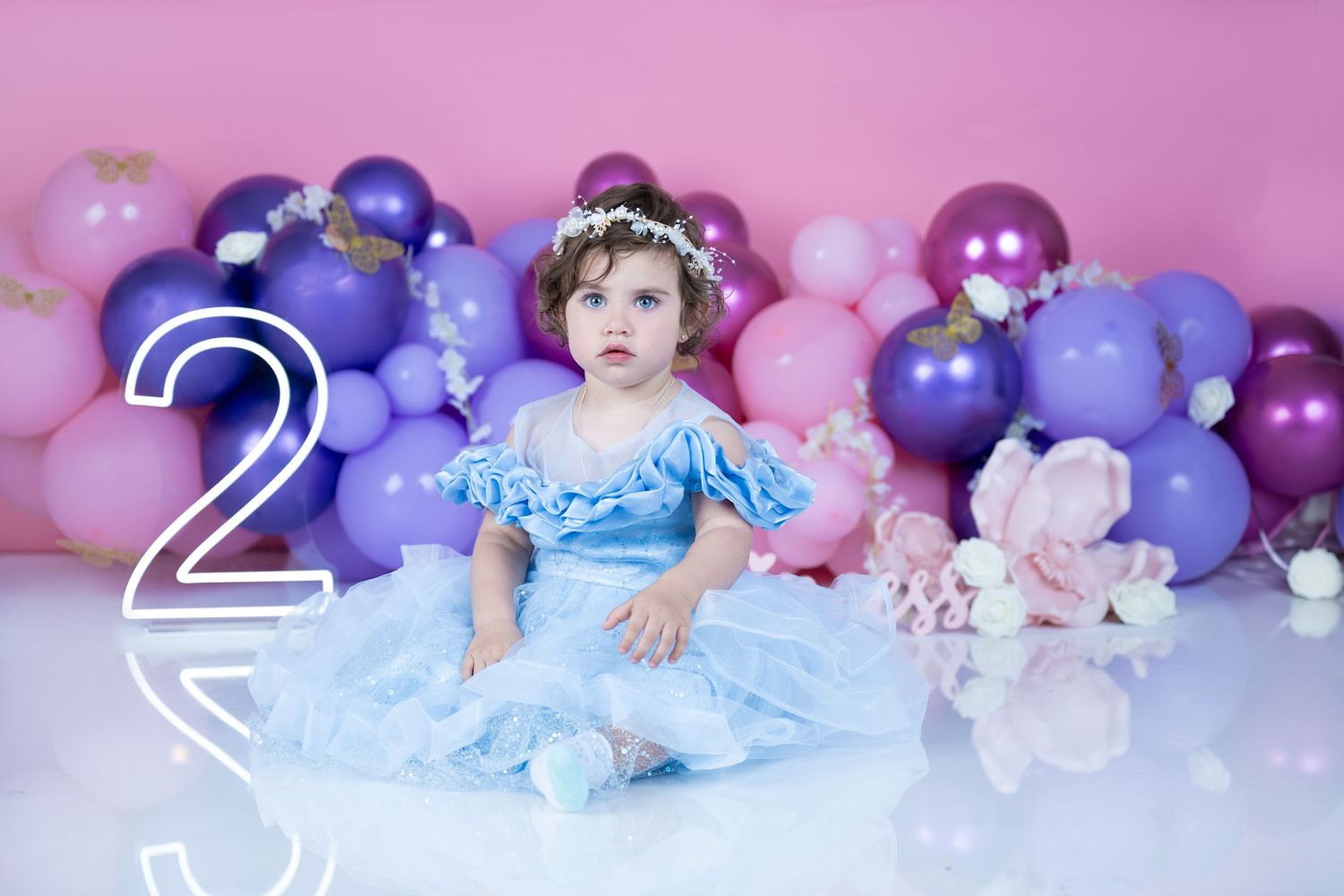 Second birthday portrait with purple balloon arch and blue princess dress.