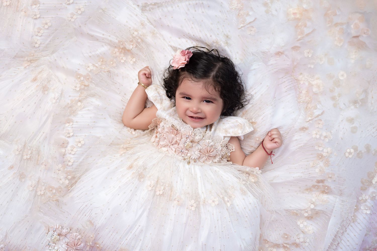 Baby wearing lace dress lays on cream textured backdrop during portrait session.