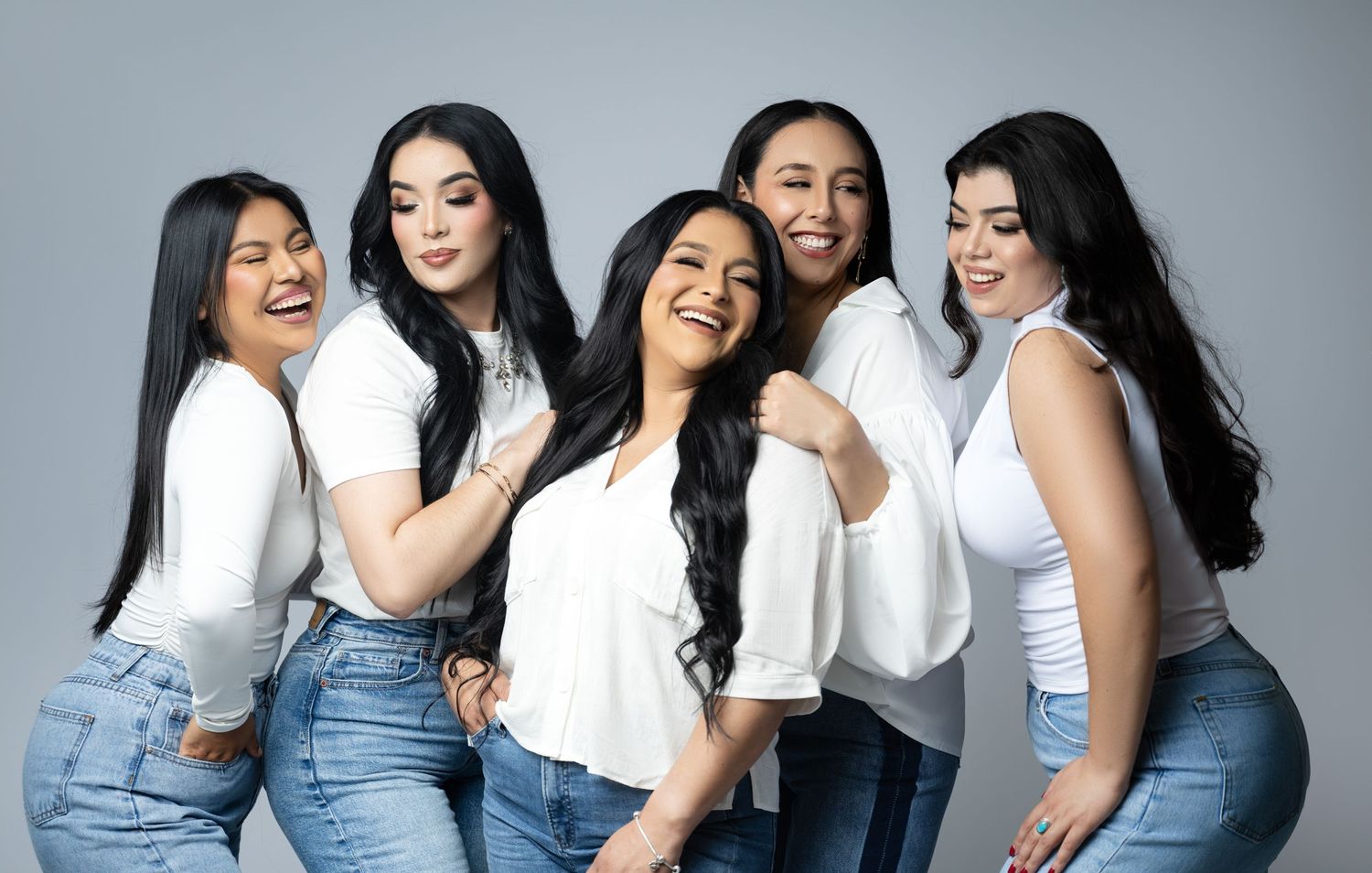Candid group photo of five people in white tops and jeans laughing together.