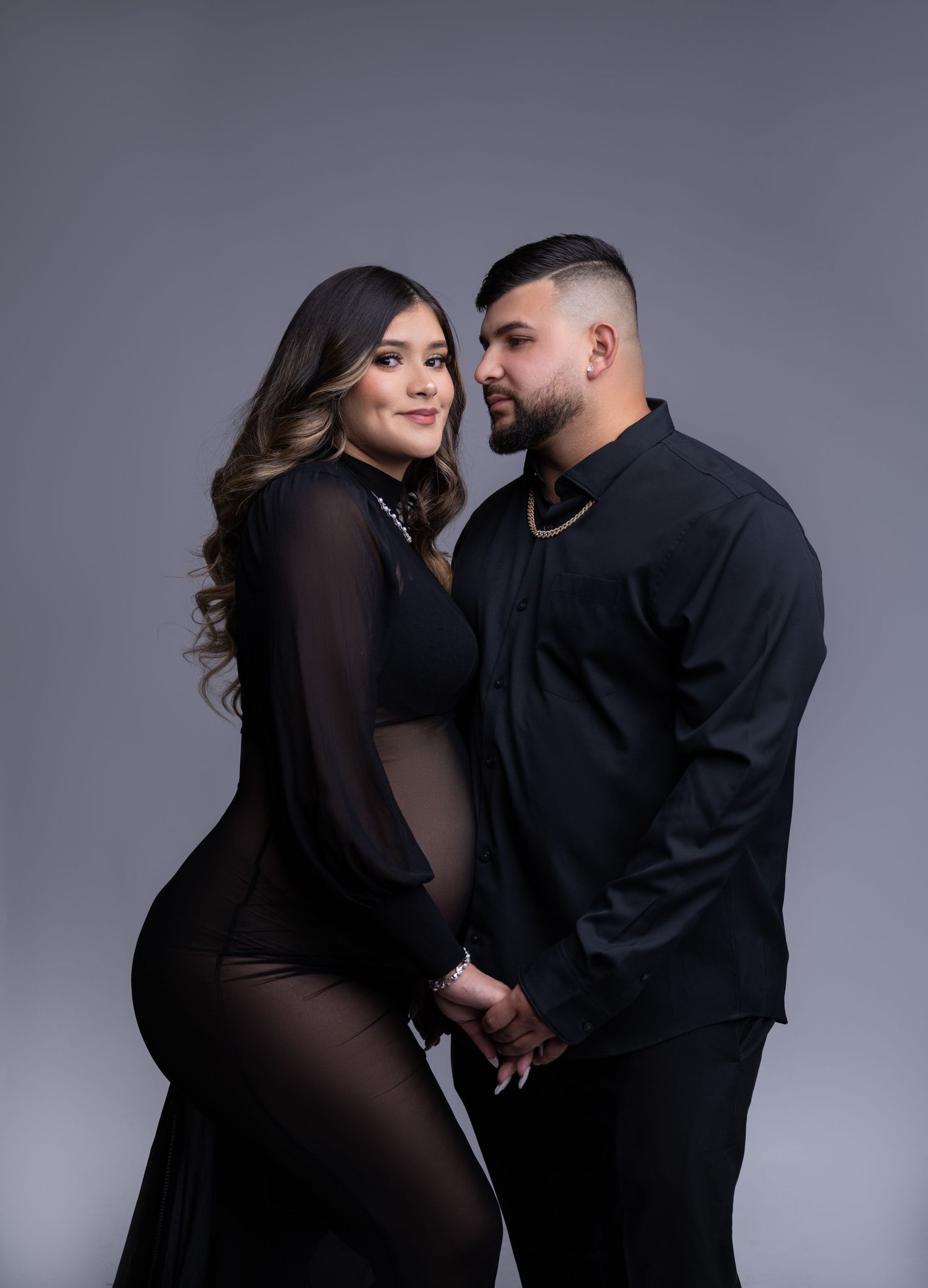 Intimate maternity portrait of couple in matching black outfits against studio backdrop.