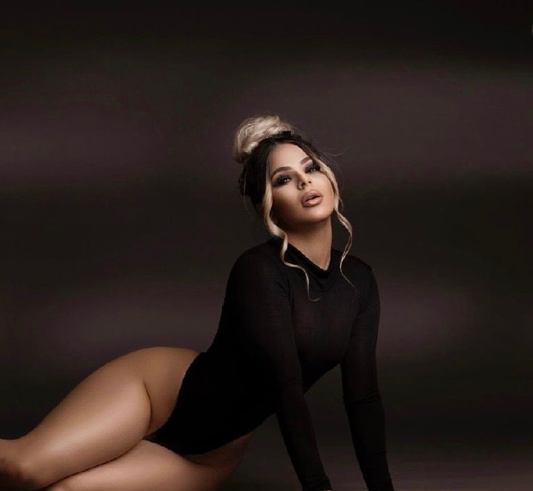 Woman in black bodysuit posing elegantly against dark background with dramatic lighting.