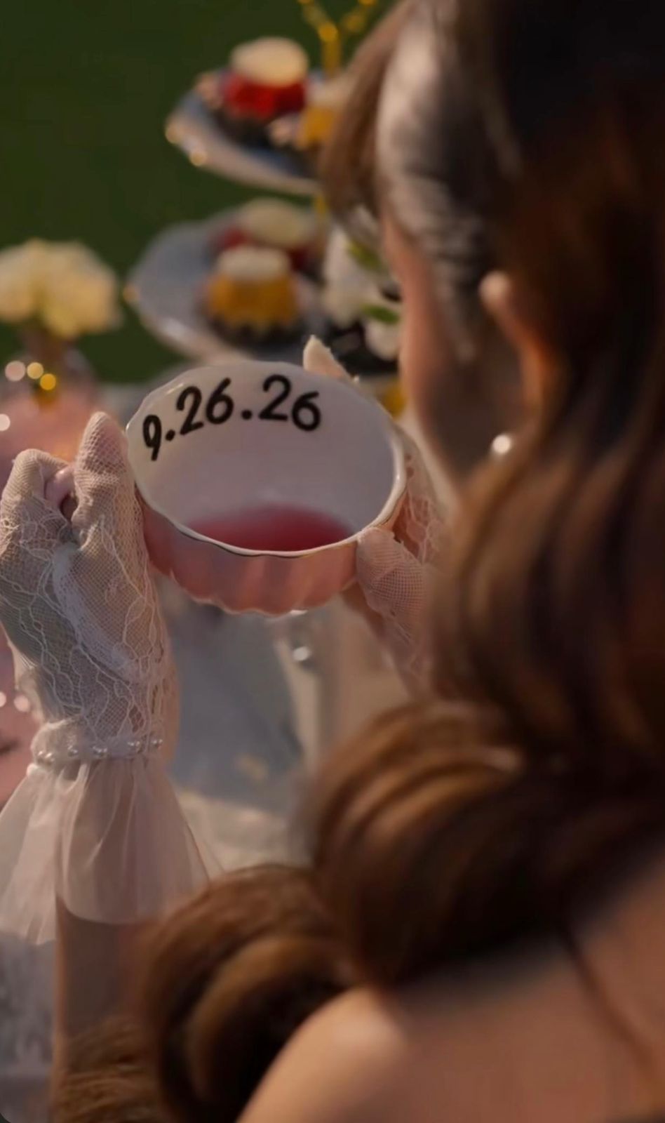 Woman in white lace gloves holding a pink cocktail glass etched with the date 9.26.26 at an elegant party.