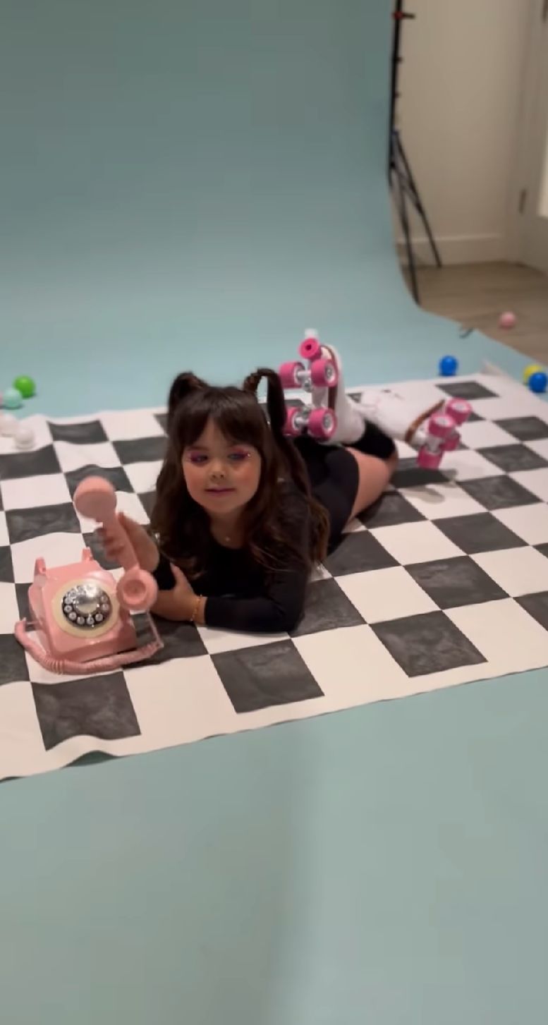 Vintage pink rotary telephone on black and white checkered floor with scattered decorative elements.