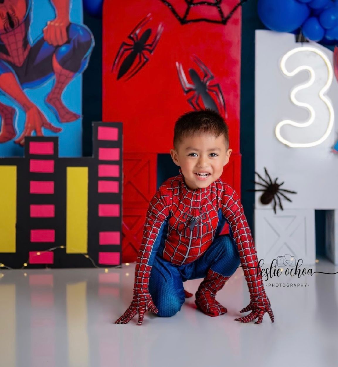 A Spider-Man themed birthday photoshoot setup with cityscape backdrop, spider decorations, and number 3 display.