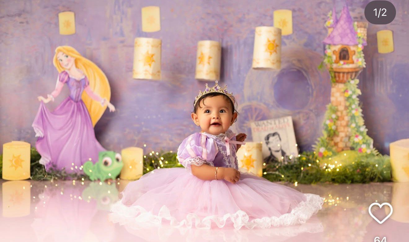 Baby girl in purple tutu dress with tiara poses in Rapunzel-themed photo shoot with Disney princess backdrop.