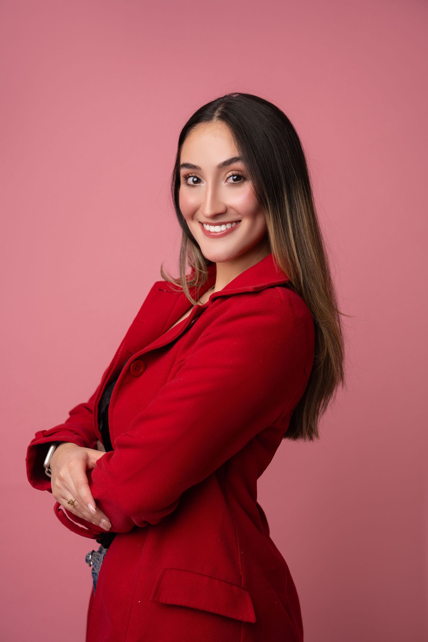 Professional portrait of person in red blazer against pink background.
