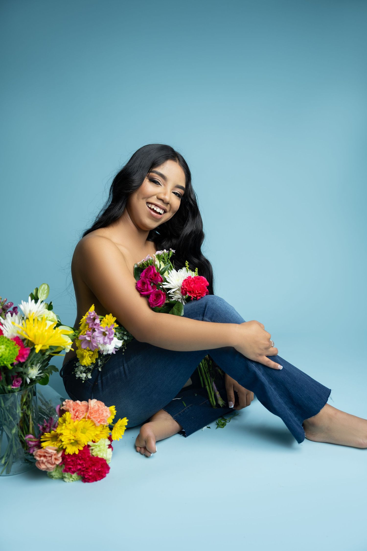 Relaxed pose with fresh floral arrangements in mason jars against turquoise studio backdrop.