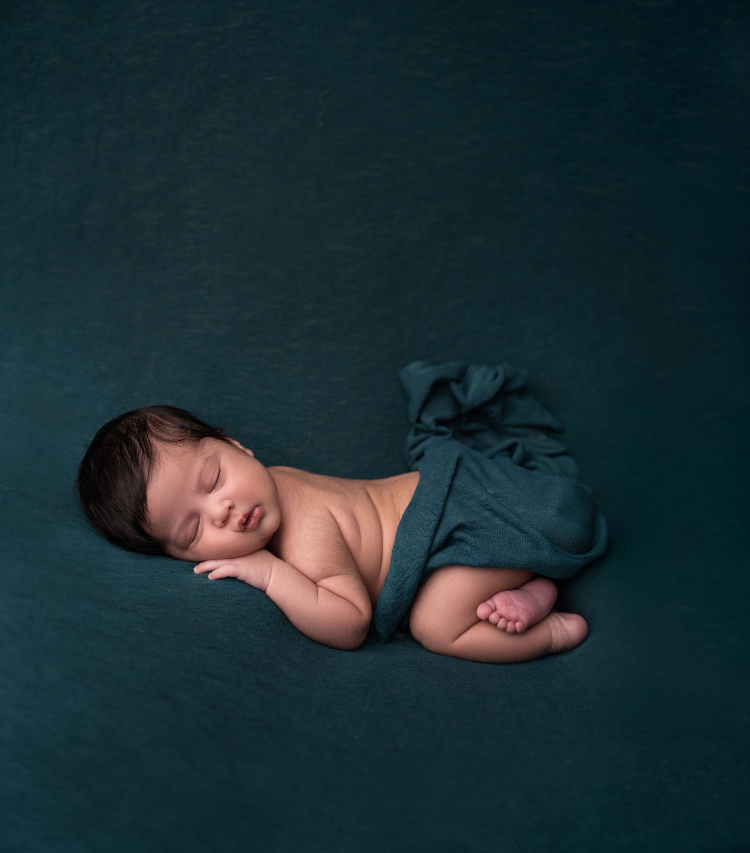 Peaceful sleeping newborn on dark teal backdrop in minimalist style.