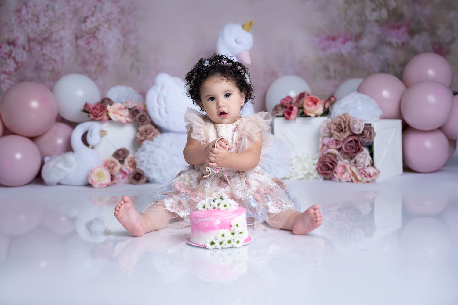 Pink balloon and floral backdrop with birthday cake in foreground for celebration photo.