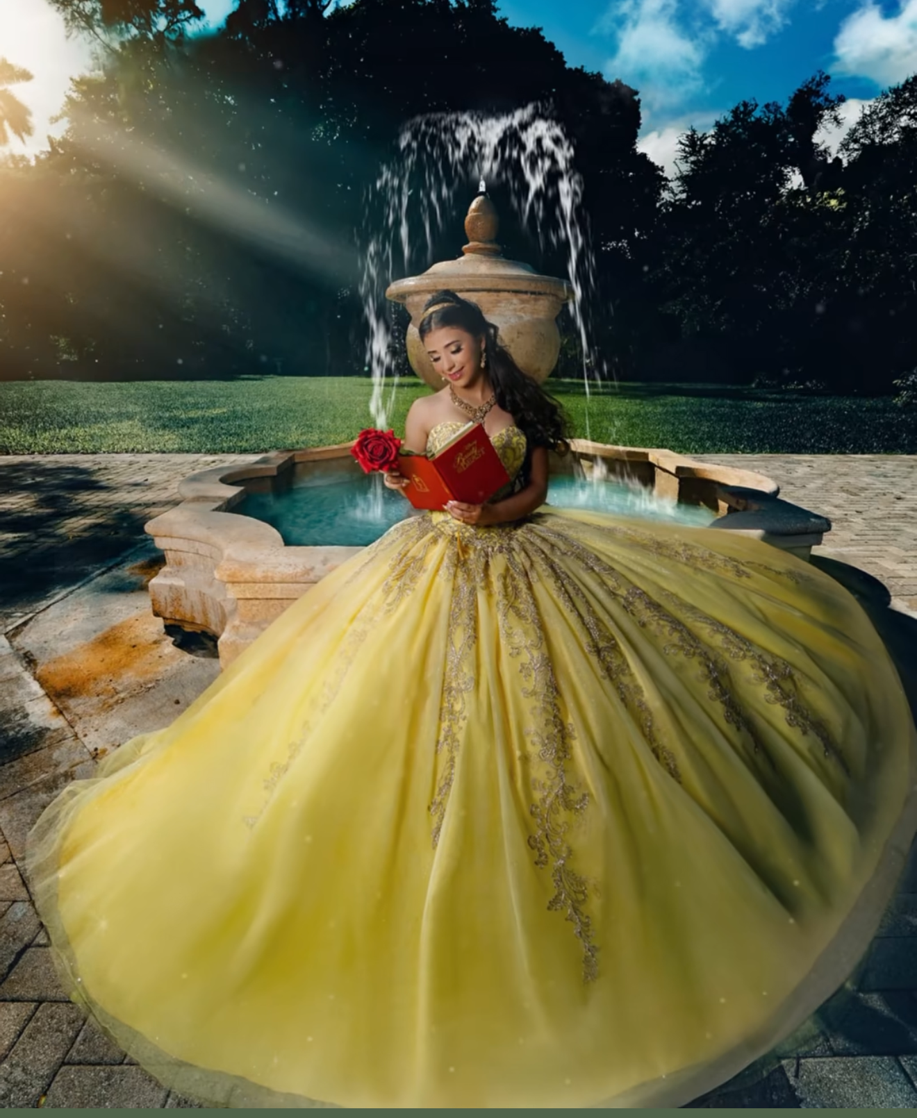 Young woman in a stunning yellow ball gown poses by a fountain, holding red roses in a Beauty and the Beast-inspired look.