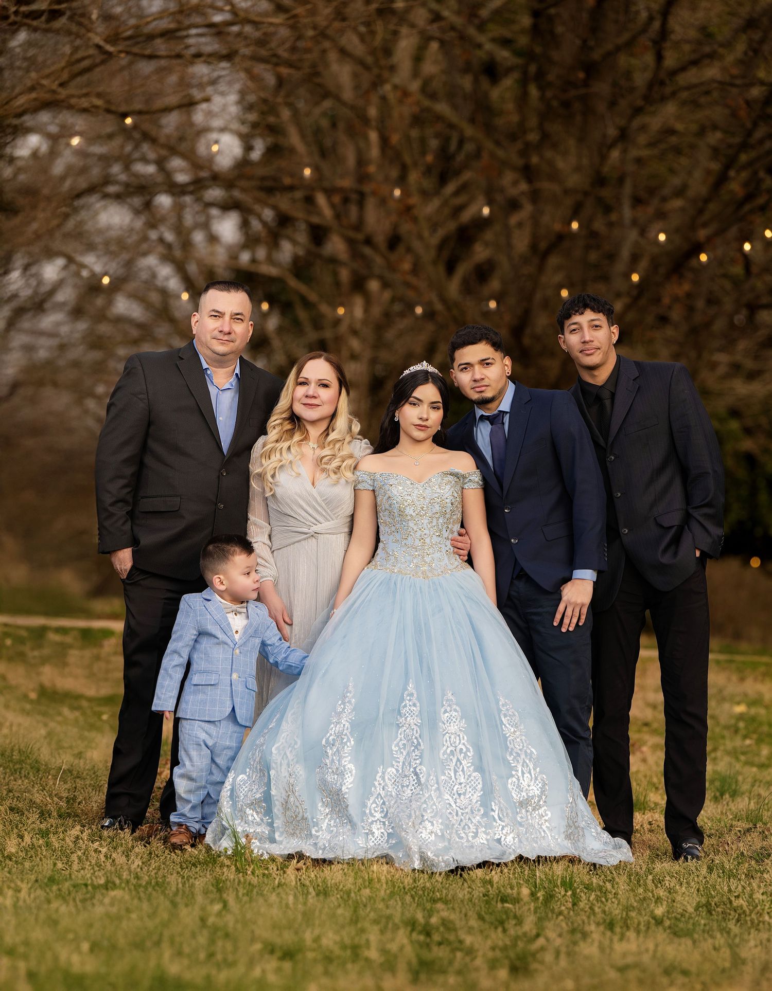 Family posing outdoors at a quinceañera celebration, featuring a girl in a light blue ball gown with lace details.