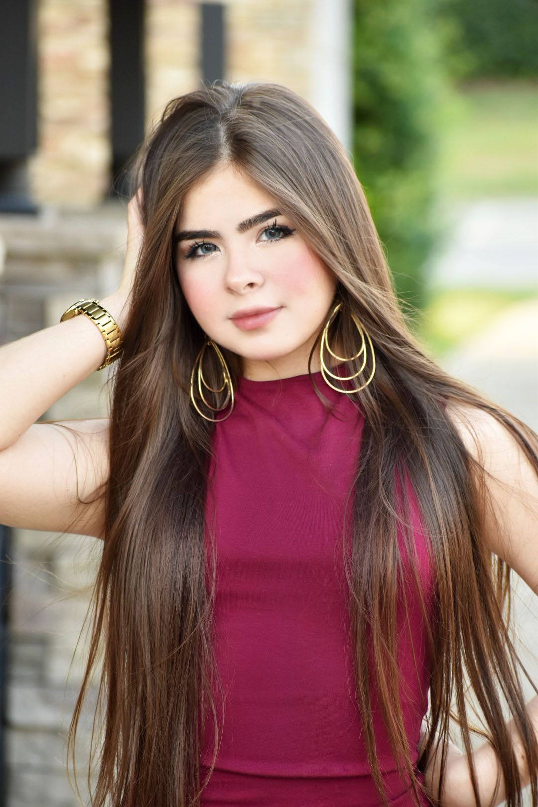 Fashion portrait wearing burgundy top and gold hoop earrings with styled long hair.