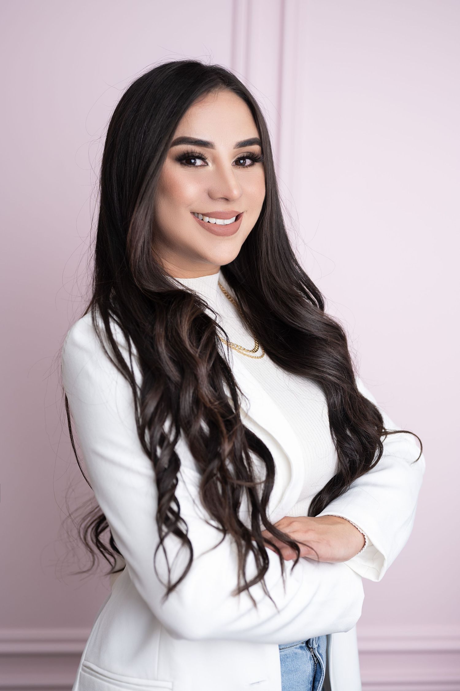Professional portrait against pink background featuring white blazer and casual denim.