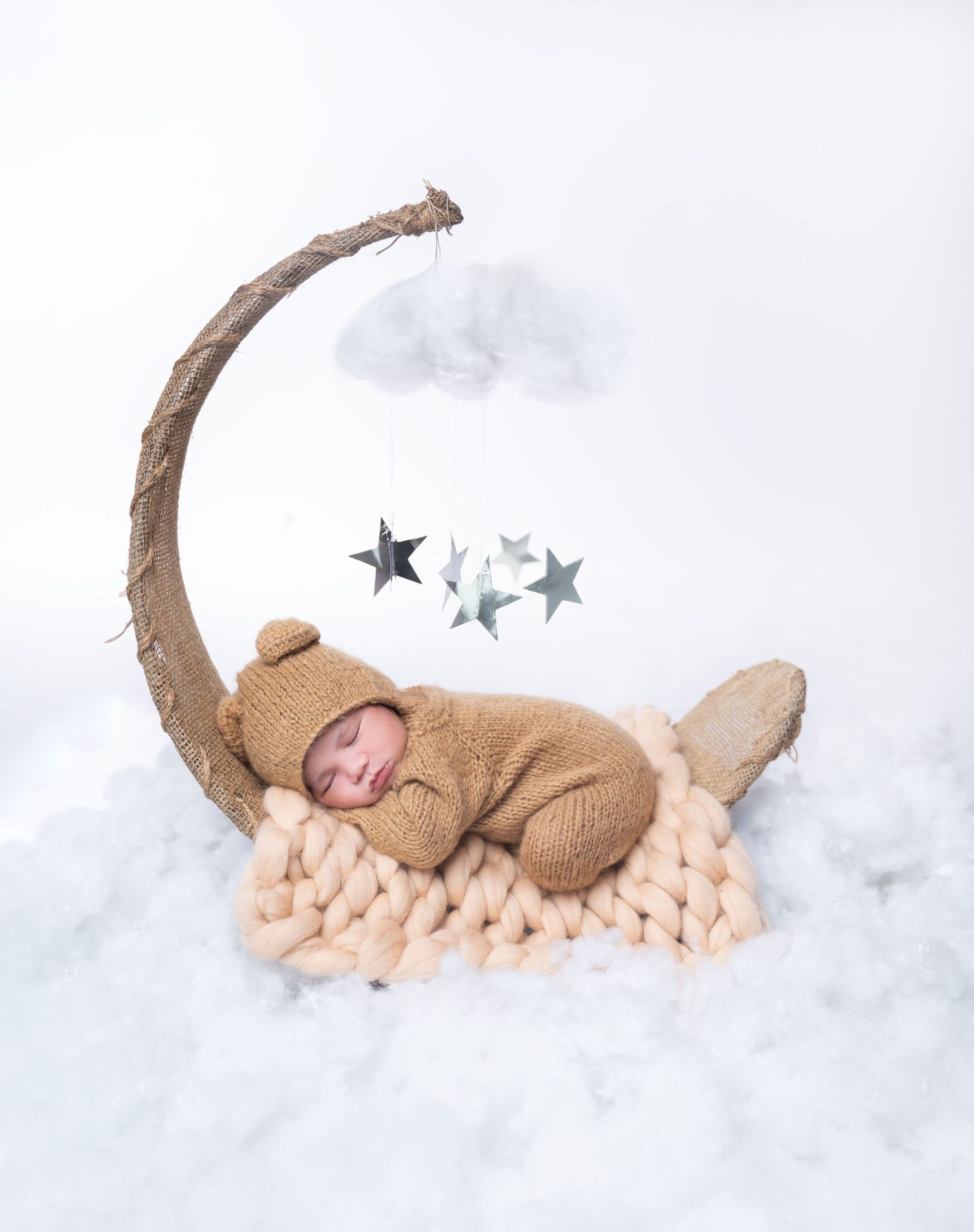 Dreamy newborn photography setup with crescent moon prop and stars on cloudy background.