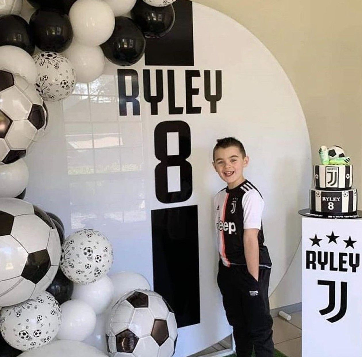 Boy named Ryley celebrates his 8th birthday with a Juventus soccer-themed party featuring balloons and a decorated cake.