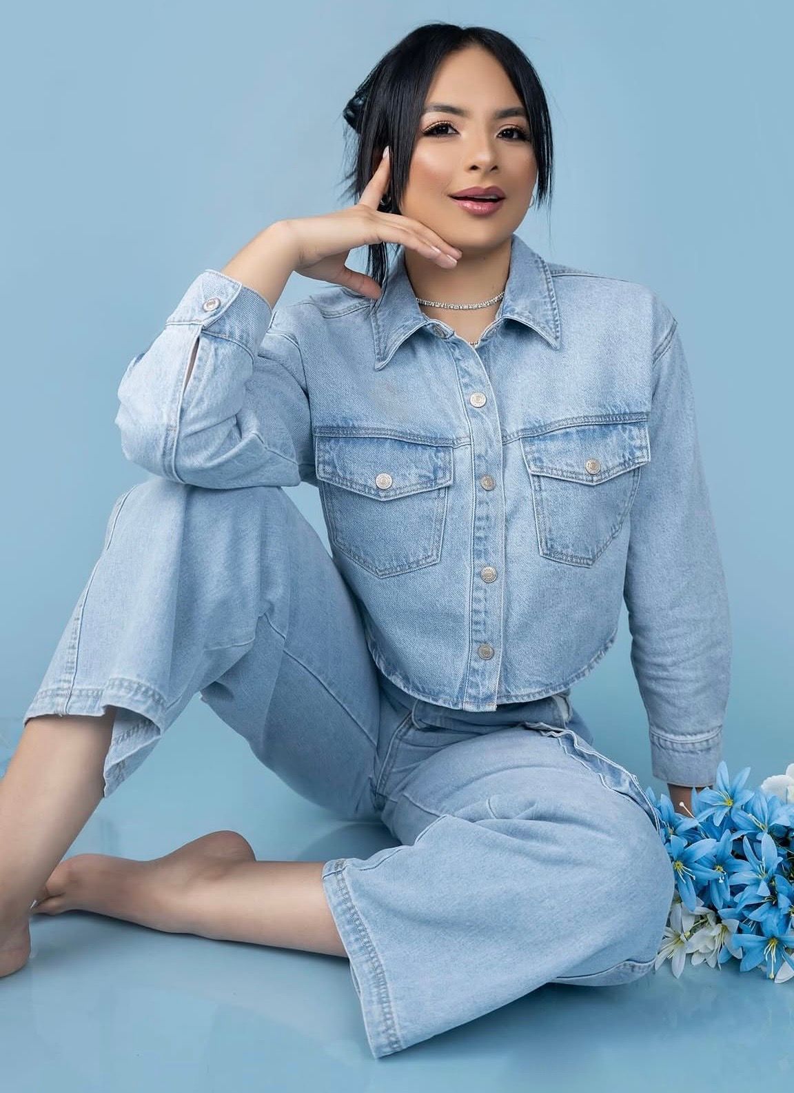 Woman in light wash denim jacket and wide-leg jeans sitting on floor with blue flowers on blue background.