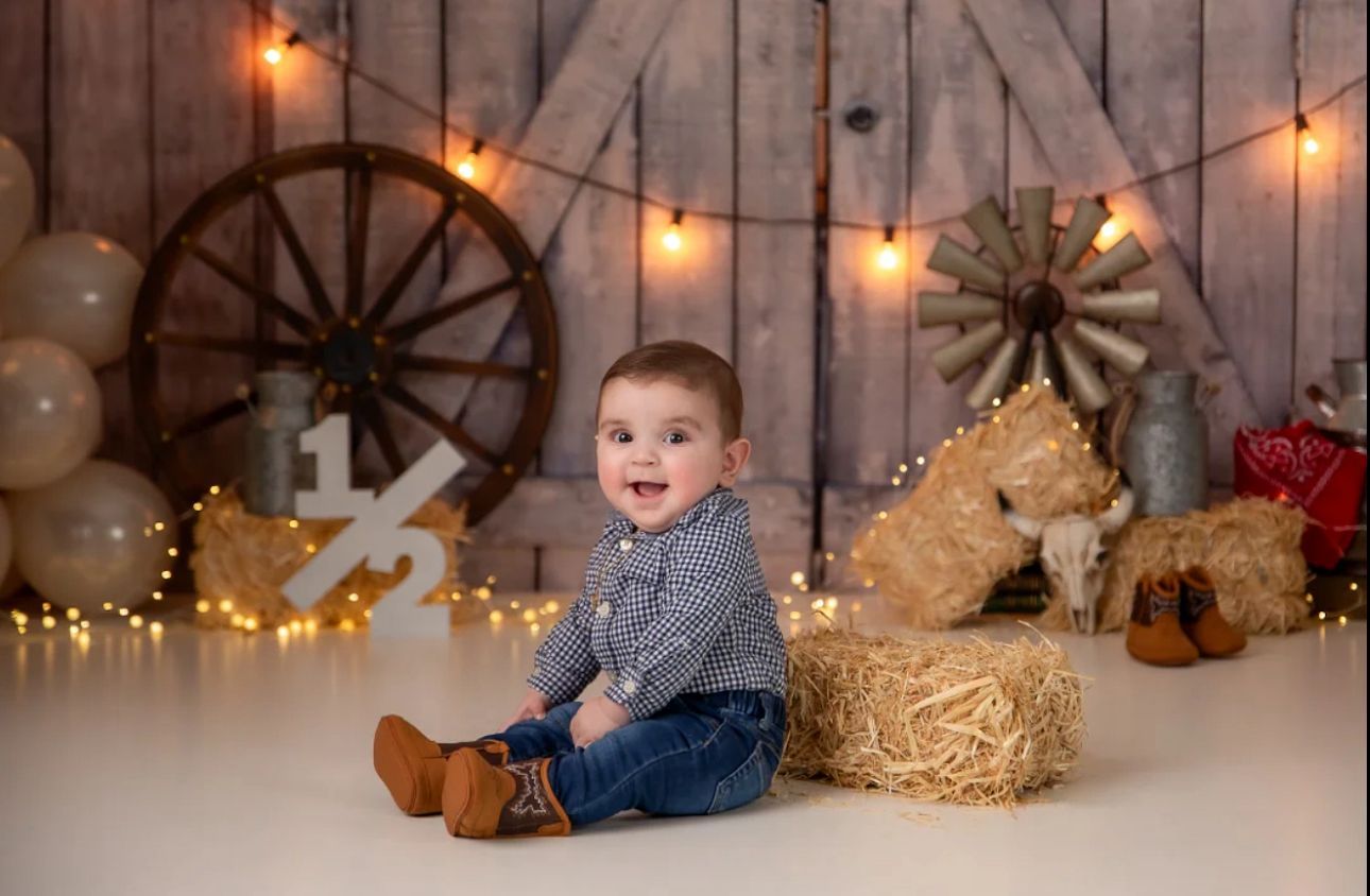 Rustic holiday photo setup with wooden wagon wheel, string lights, and cozy decor against barn wood wall.