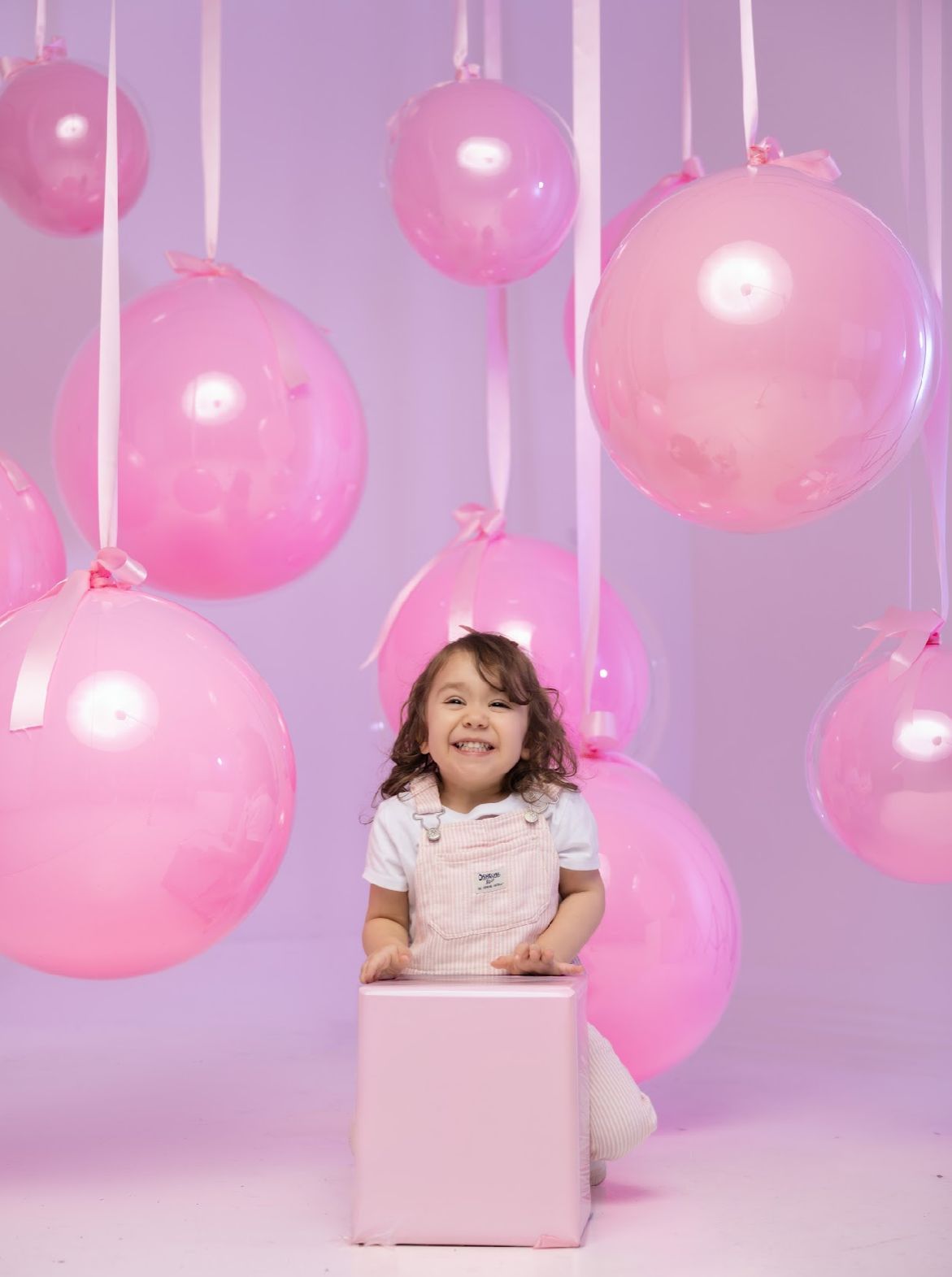 Whimsical pink balloon decorations hanging from strings against a soft purple background.