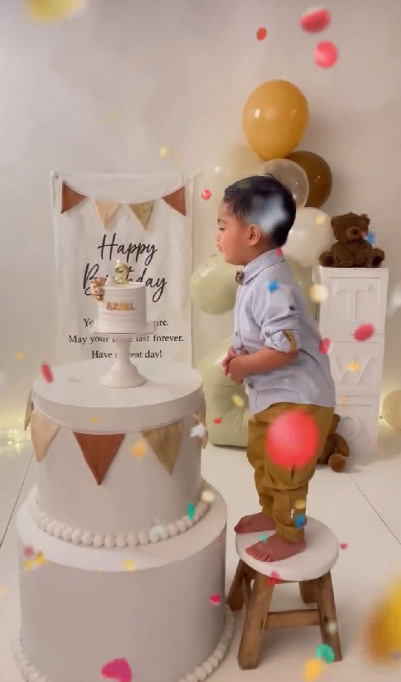 A white tiered birthday cake display with balloons and bunting decorations in a festive setting.