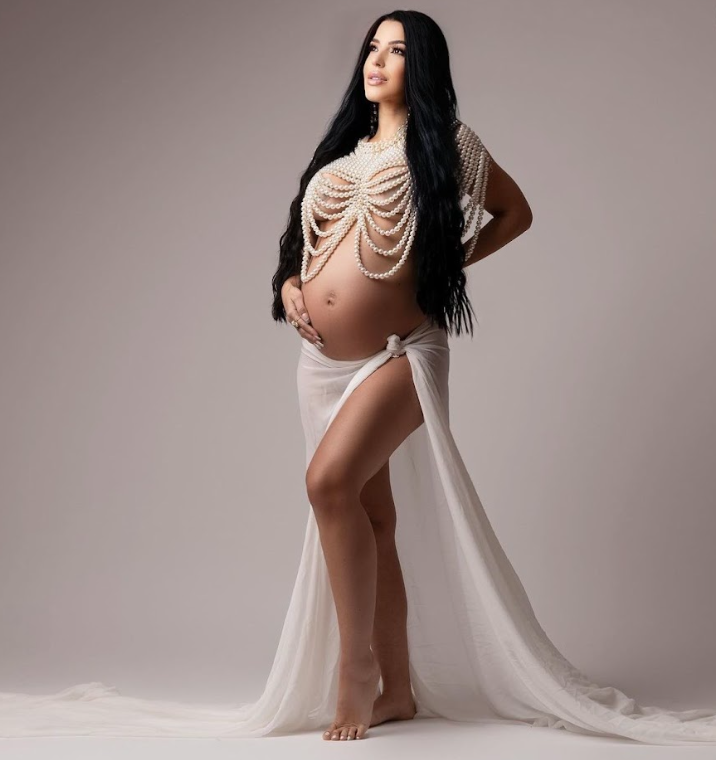 Artistic maternity photoshoot with flowing white fabric and nude silhouette against neutral backdrop.