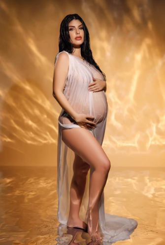 Artistic maternity photoshoot with flowing white fabric against warm golden backdrop.