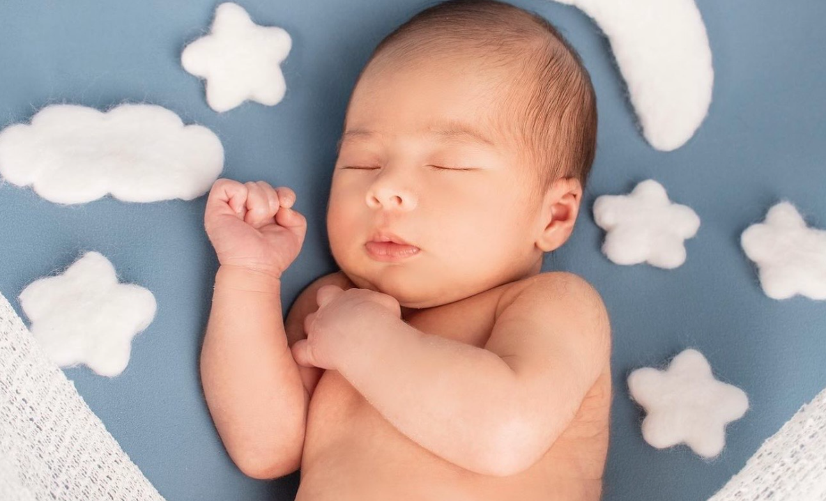 Sleeping newborn baby on soft blue background with white cloud decorations.