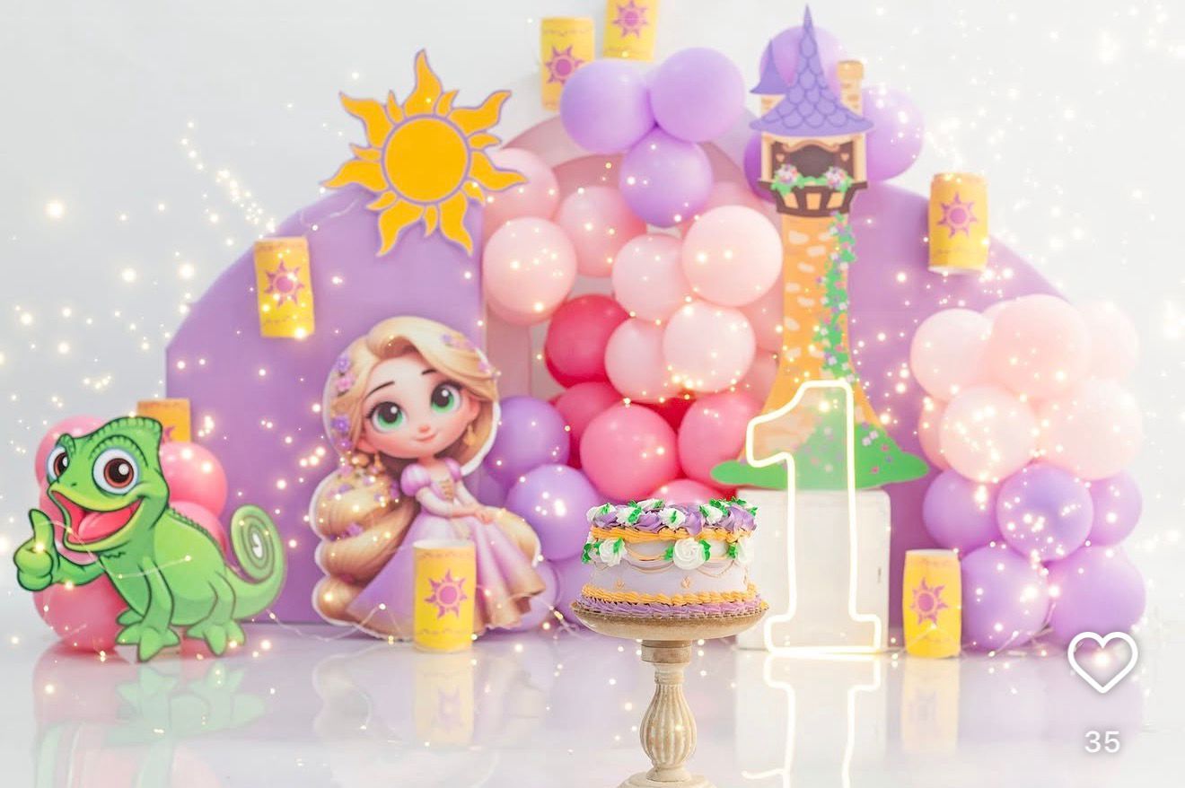 Rapunzel-themed first birthday party setup with balloon arch, princess cutout, Pascal the chameleon, and a decorated cake.