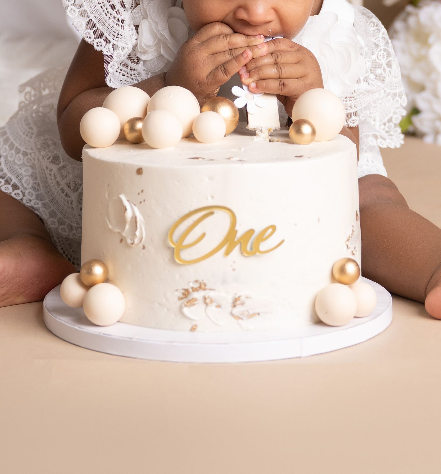 A white birthday cake decorated with gold accents and pearl-like spheres.