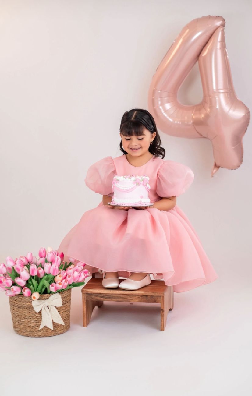 Pink birthday photo setup with number 4 balloon, wooden stool, and pink tulip flowers arranged in a studio setting.