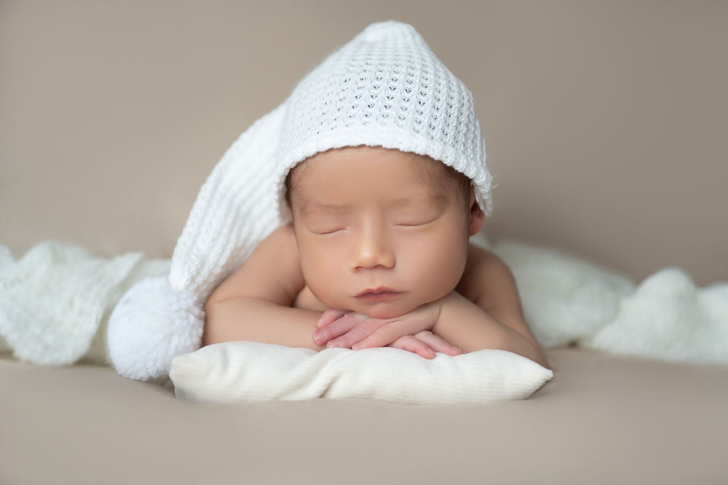 Peaceful newborn sleeping on white pillow wearing knit white hat.