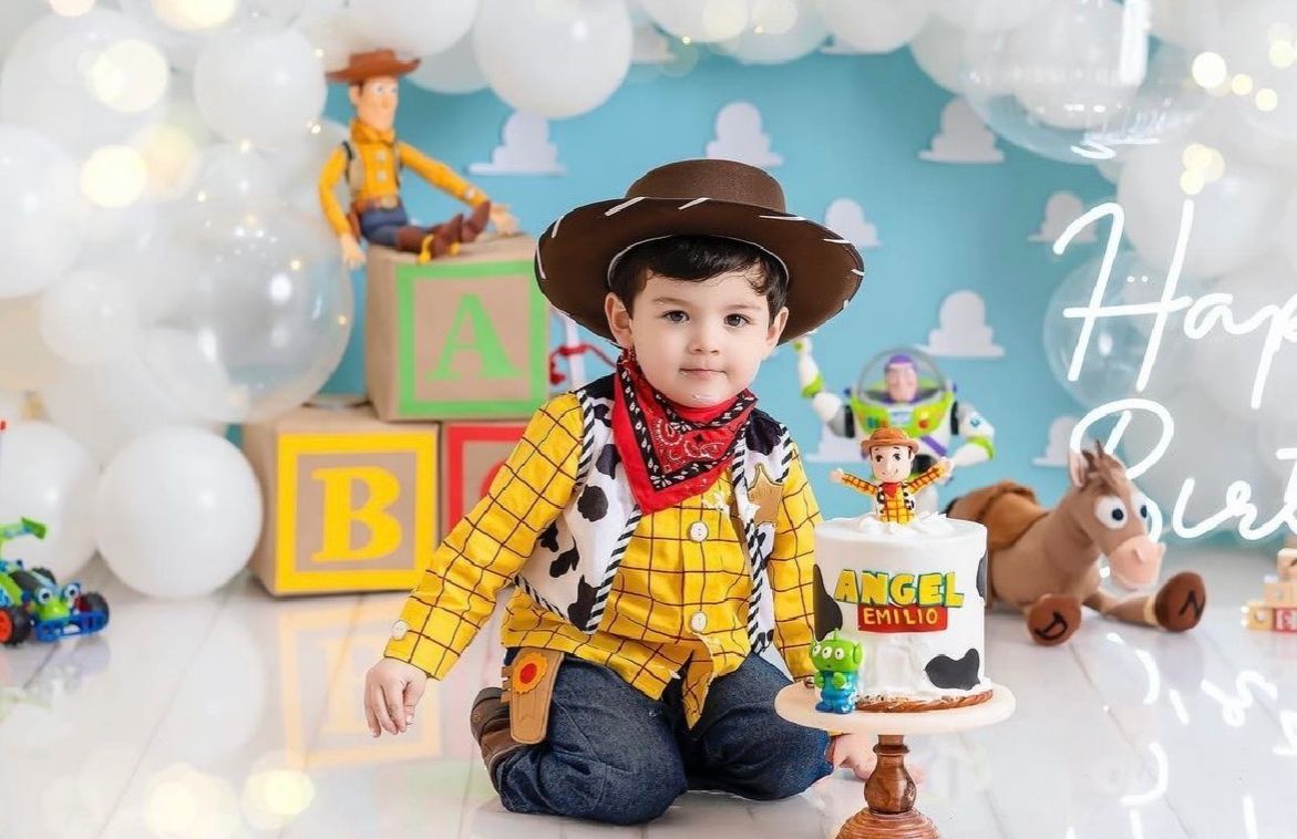 A child dressed as Woody from Toy Story poses in a themed photoshoot with toys and decorative blocks.