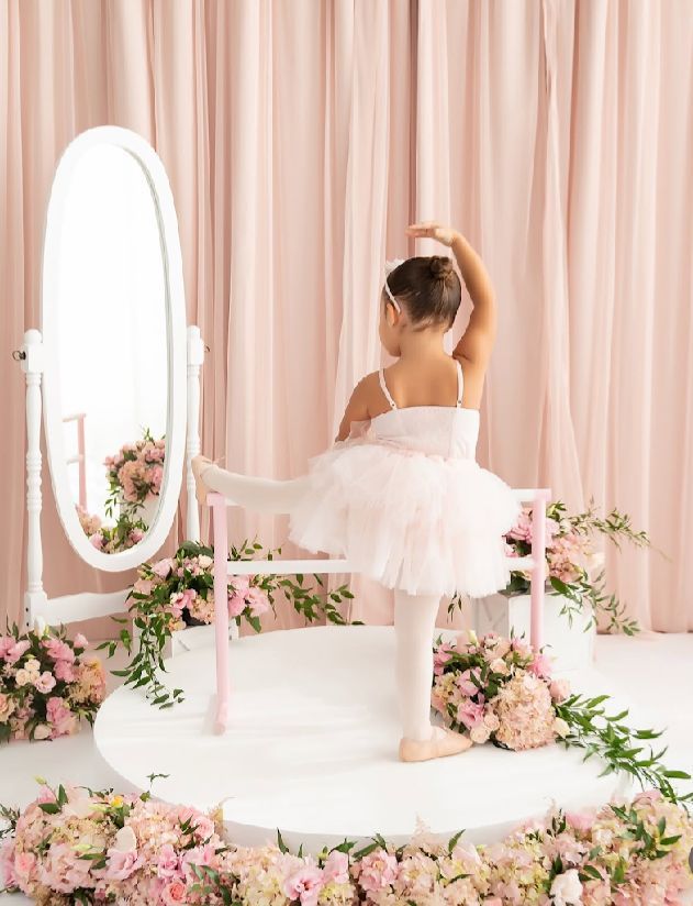 Elegant pink and white vanity area with oval mirrors and floral decorations against a soft draped curtain background.