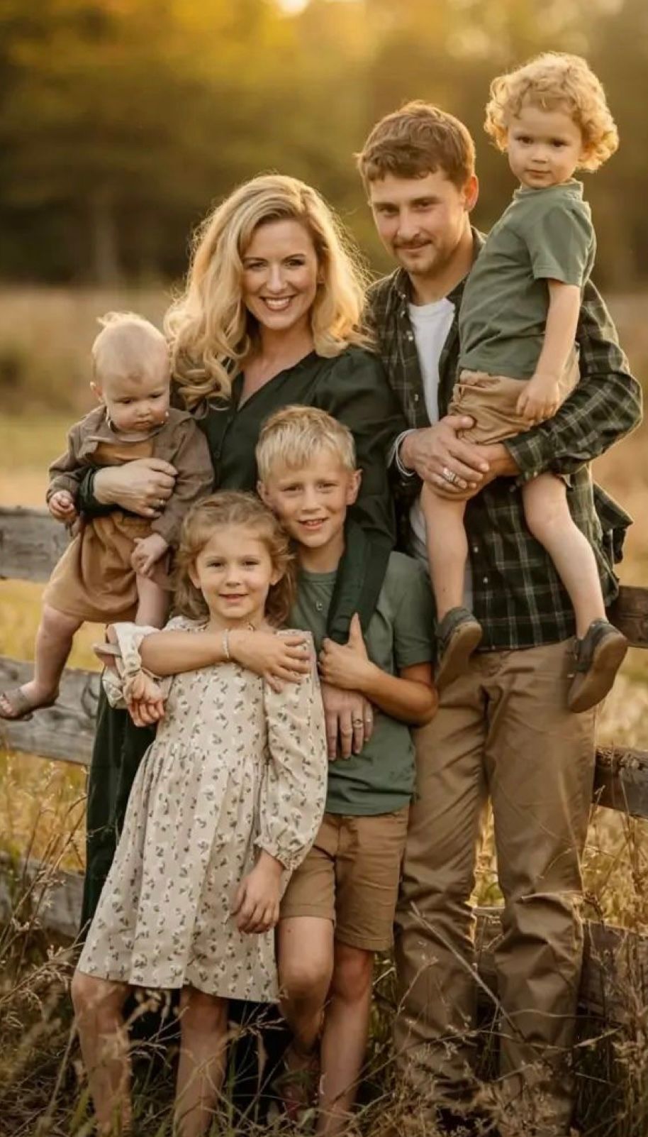 A family in coordinated earthy tones poses together outdoors during golden hour in a grassy field.