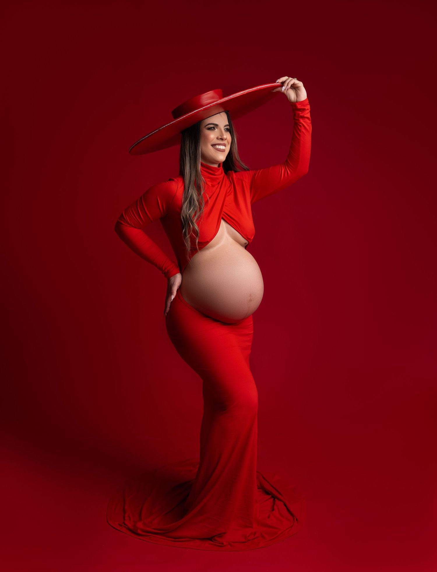Maternity photo series showing a woman in a flowing red dress against a deep crimson background in artistic poses.