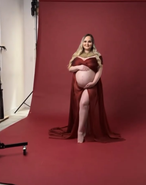 Maternity photo shoot in a studio with burgundy walls and floor featuring a figure in a pink dress.