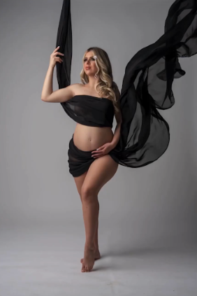 Artistic maternity photo with flowing black fabric against grey background creating dramatic movement and elegance.
