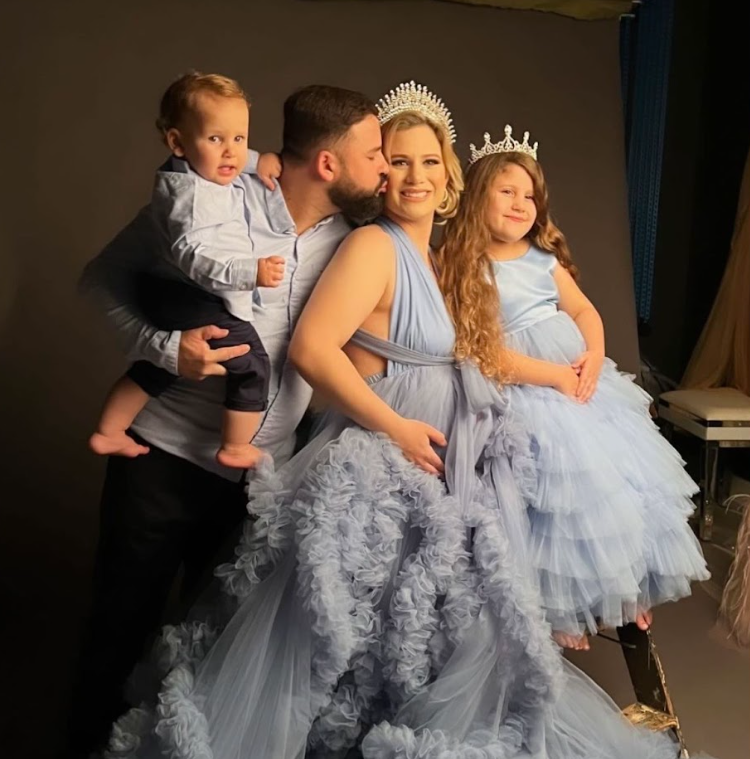 Family in coordinating light blue tulle dresses and formal wear embrace during special occasion photoshoot.