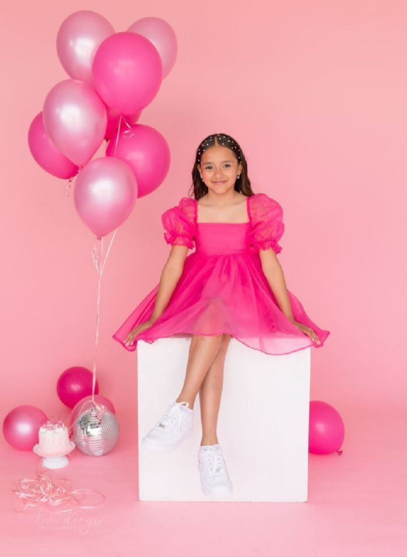 Pink balloons and white platform create a whimsical photo setup against a rosy backdrop.