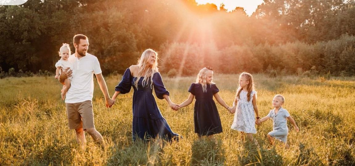 A group walks through a golden sunlit meadow during sunset creating a silhouetted panoramic image.