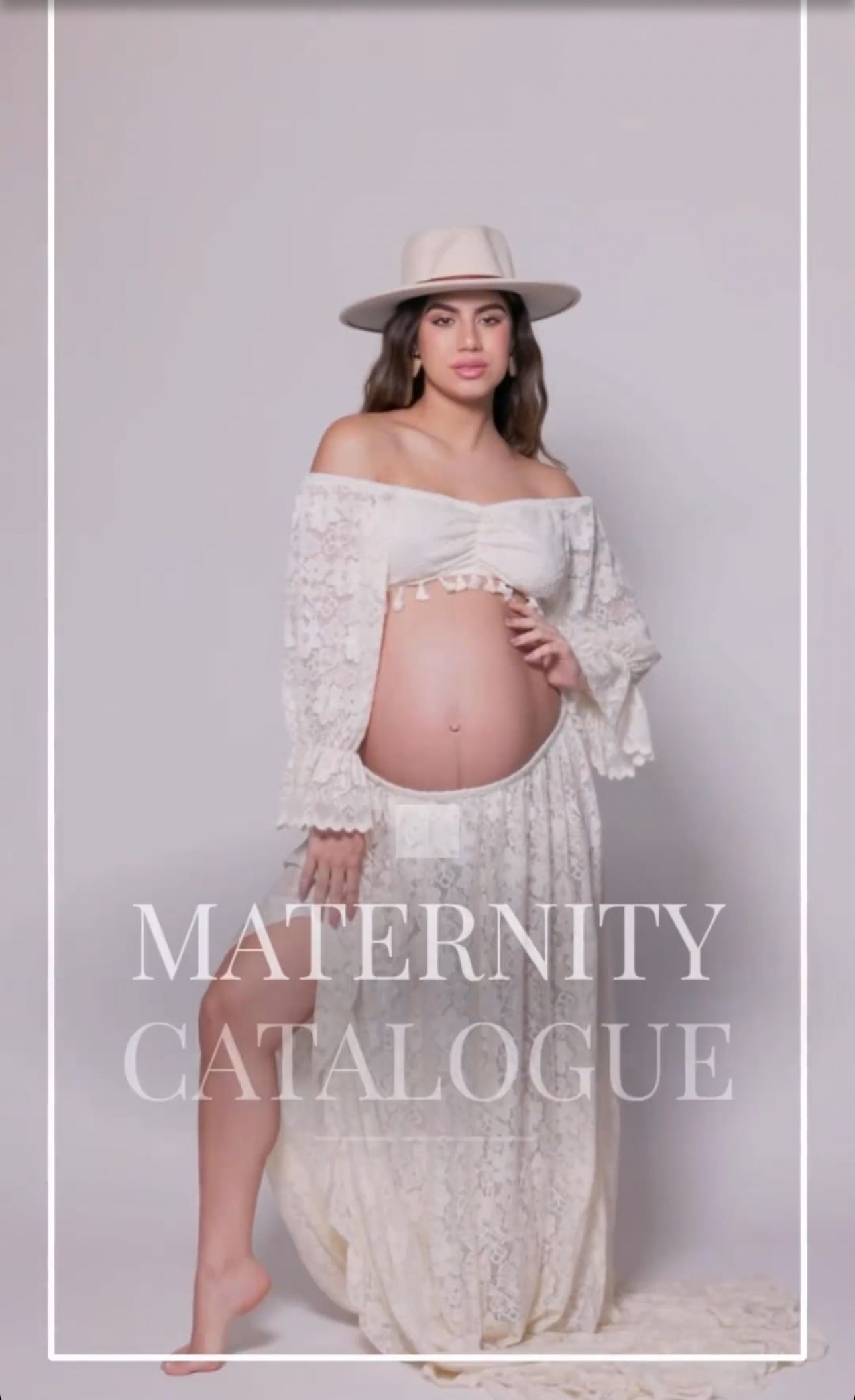 Maternity catalogue photo of pregnant woman in white lace dress and wide-brim hat.