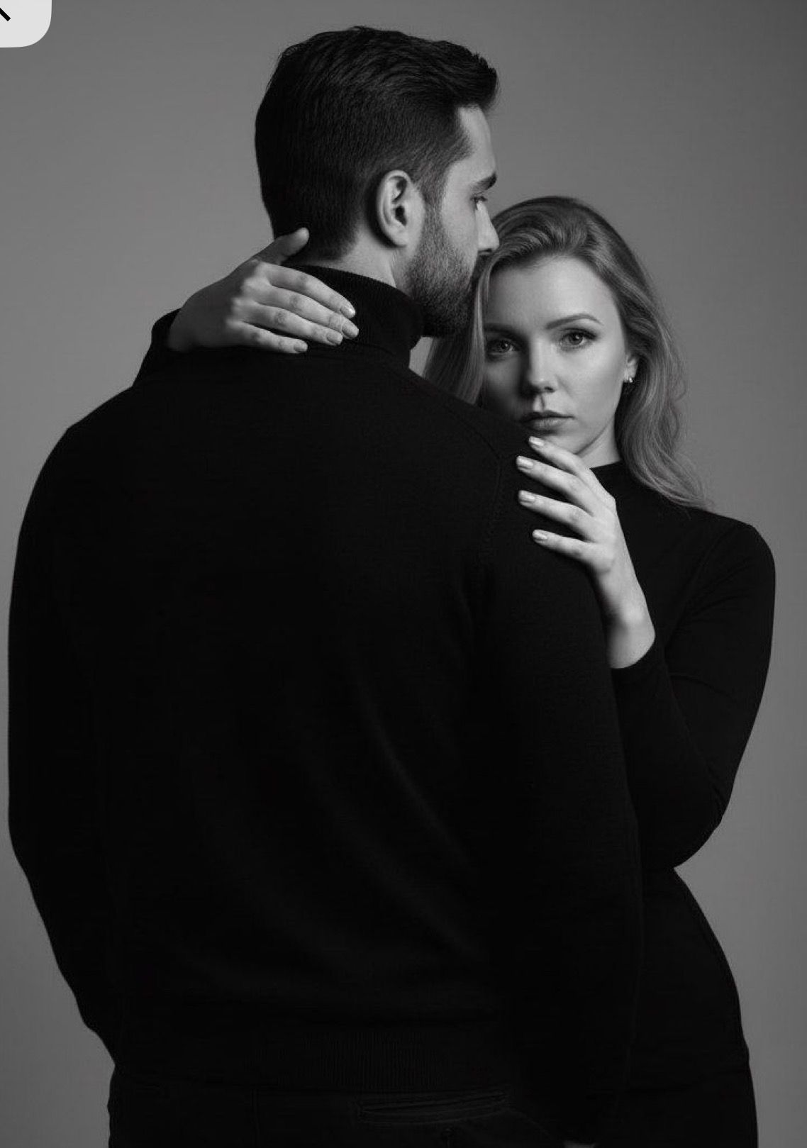 Black and white photo of a couple embracing, woman in black turtleneck gazing at camera while holding mans neck.