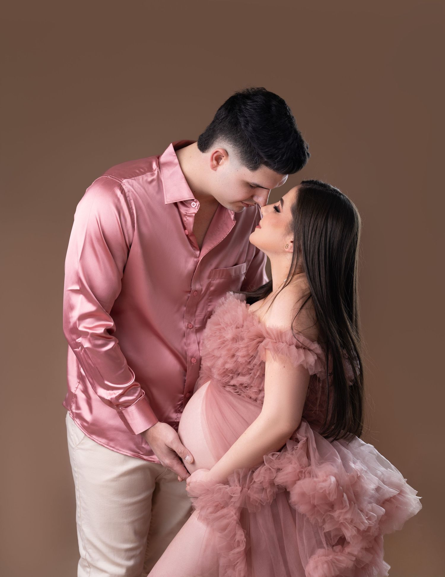 Romantic maternity portrait with couple in pink and beige formal attire.