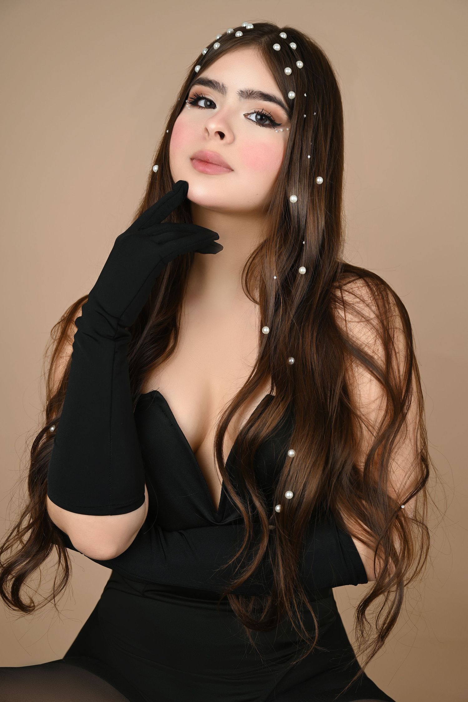 Glamour portrait in black dress and gloves with pearl hair accessories against beige backdrop.