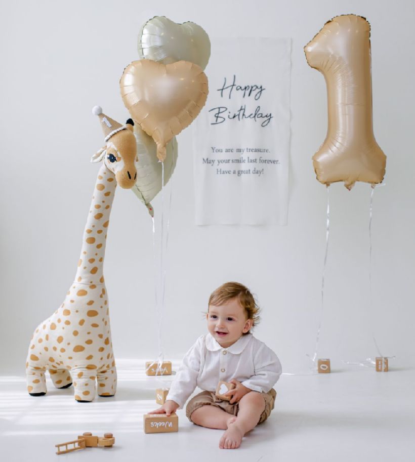 A series of milestone photos showing a baby sitting next to a giraffe plush toy and gold balloons against a white backdrop.