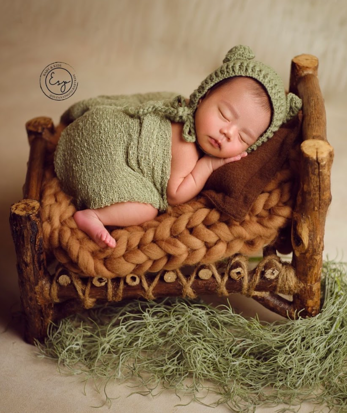 Newborn sleeping peacefully on rustic wooden prop with green knit outfit and natural Spanish moss accents.