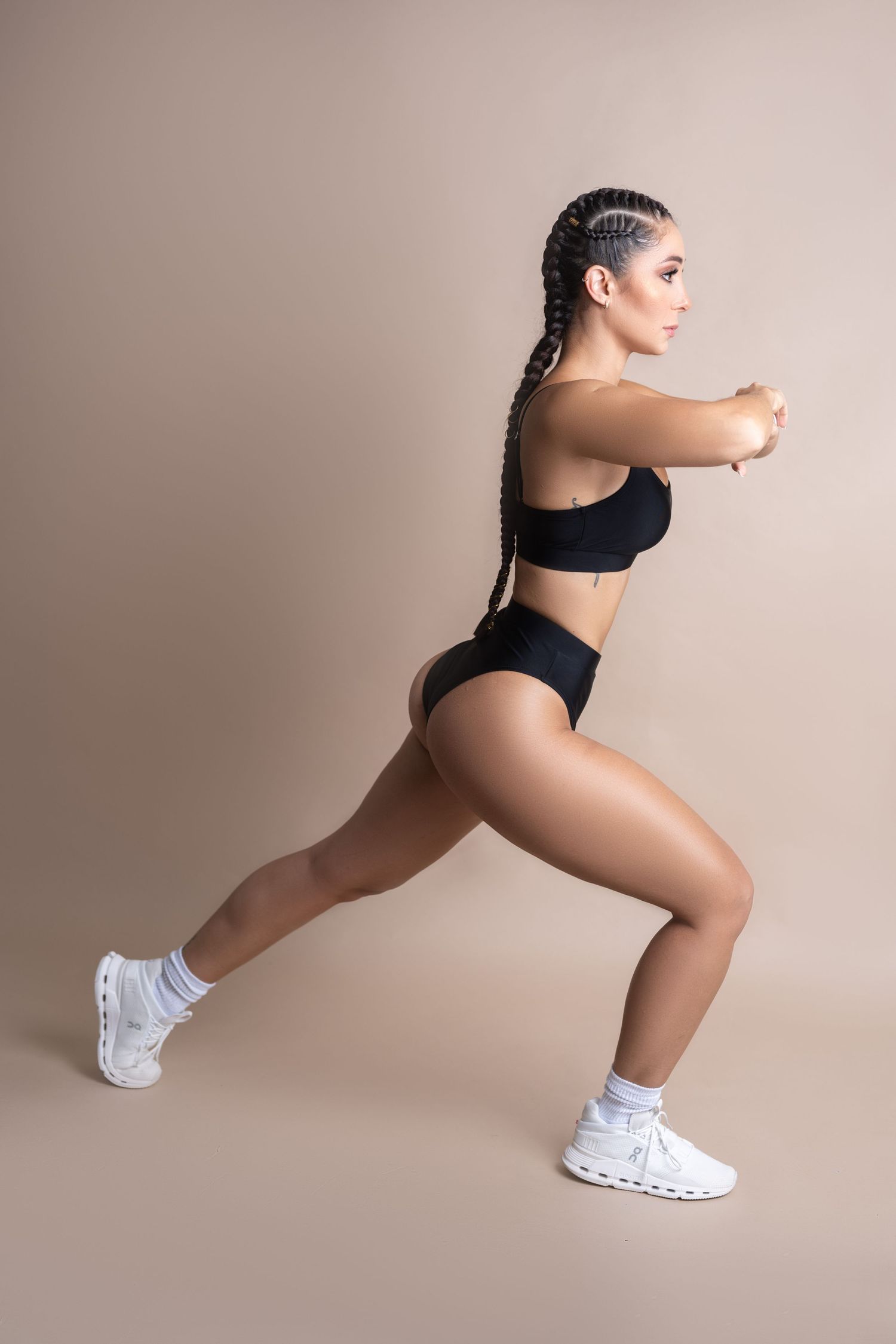 Woman in black workout attire doing lunges against neutral studio backdrop.