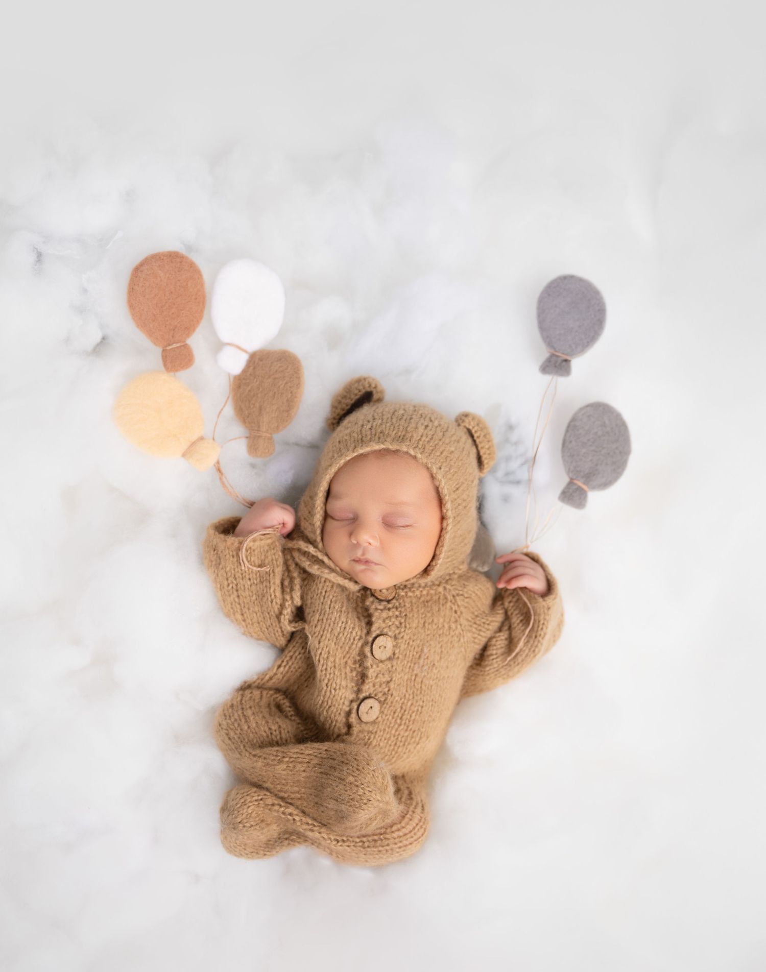 Sweet sleeping baby in bear outfit with floating balloon decorations.