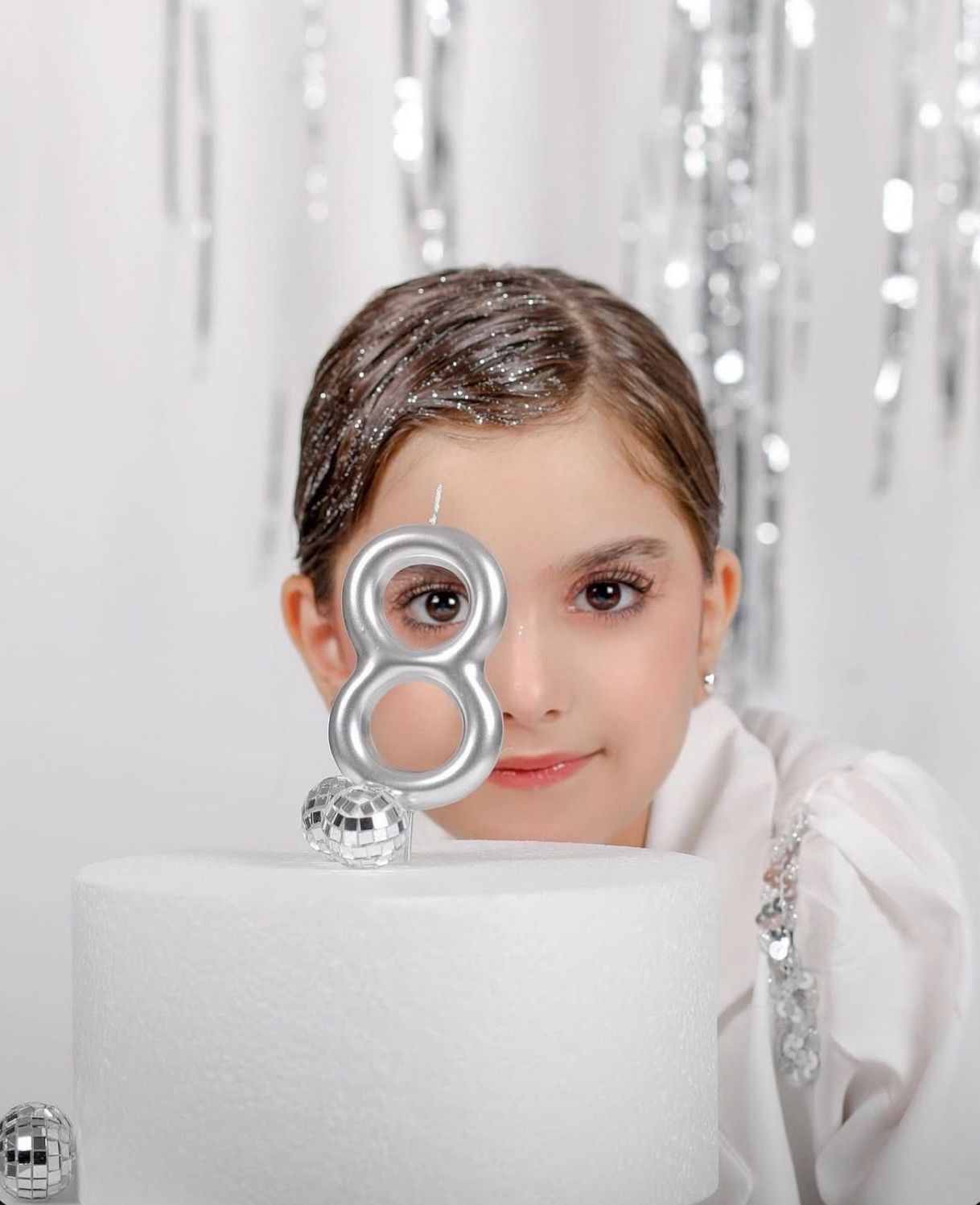 A young girl peers over a white birthday cake with a silver number 8 candle, celebrating her 8th birthday.